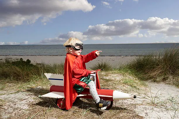 Little girl sits on a play rocket she is dressed superhero costume