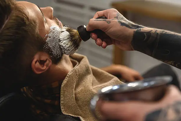 hairdresser applying shaving cream on face of man, concept of shaving