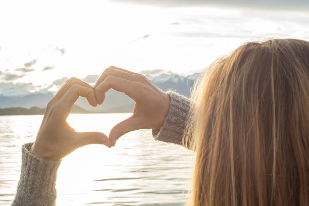 istock Female makes heart shape finger frame on lake mountain landscape 613210200