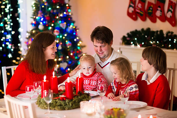 Family with children at Christmas dinner at home Big family with three children celebrating Christmas at home. Festive dinner at fireplace and Xmas tree. Parent and kids eating at fire place in decorated room. Child lighting advent wreath candle. advent candle wreath christmas stock pictures, royalty-free photos & images