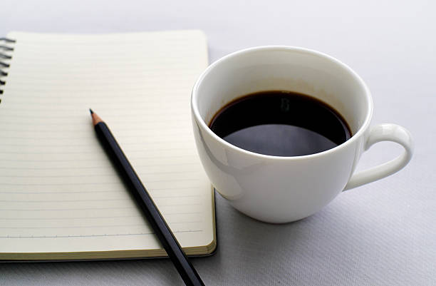 istock Coffee in white cup with Journal book and pencil 613227342