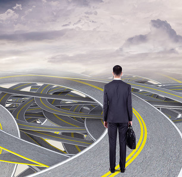 istock Confused businessman standing on tangled highway 613231598