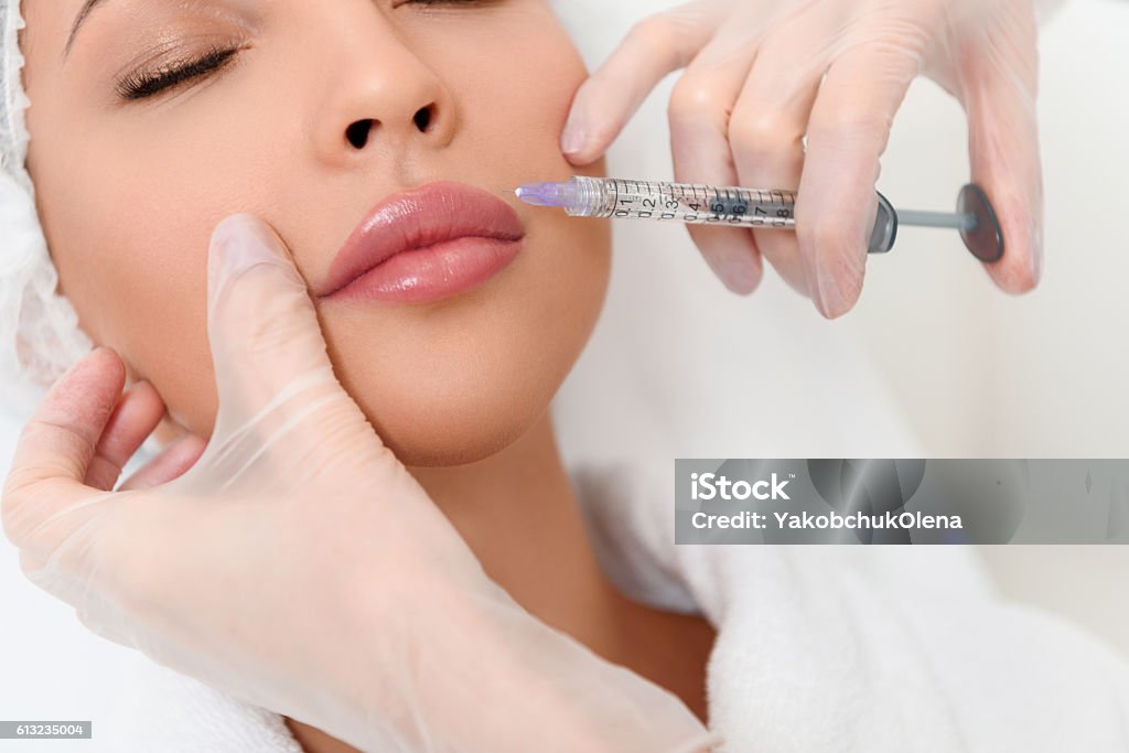 Professional cosmetologist making facial injection Close up of beautician hands in gloves injecting female lips with botox. Calm woman is lying with closed eyes Botulinum Toxin Injection Stock Photo