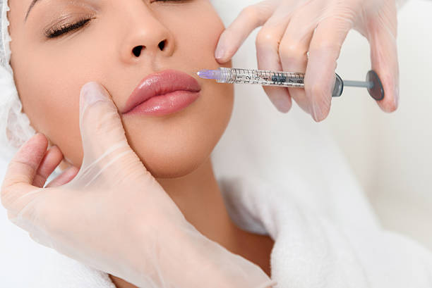 Professional cosmetologist making facial injection Close up of beautician hands in gloves injecting female lips with botox. Calm woman is lying with closed eyes plastic surgery photos stock pictures, royalty-free photos & images