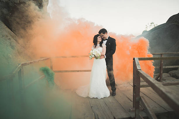 istock Wedding couple posing near rocks with colored smoke behind them 613237518