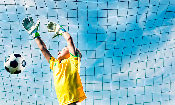 вратарь прыгает, чтобы блокировать футбольный мяч от забил гол - playing field kids soccer goalie soccer player стоковые фото и изображения