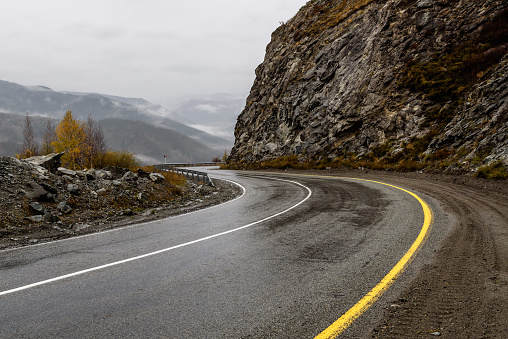 Scenic view of the hairpin bend wet winding road through the pass, part of the mountain serpentine in autumn cloudy weather with fog