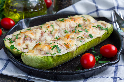 Zucchini boats stuffed with ground meet and topped with cheese on a cast iron pan, horizontal