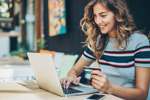 Smiling young woman holding a credit card and typing on a laptop.