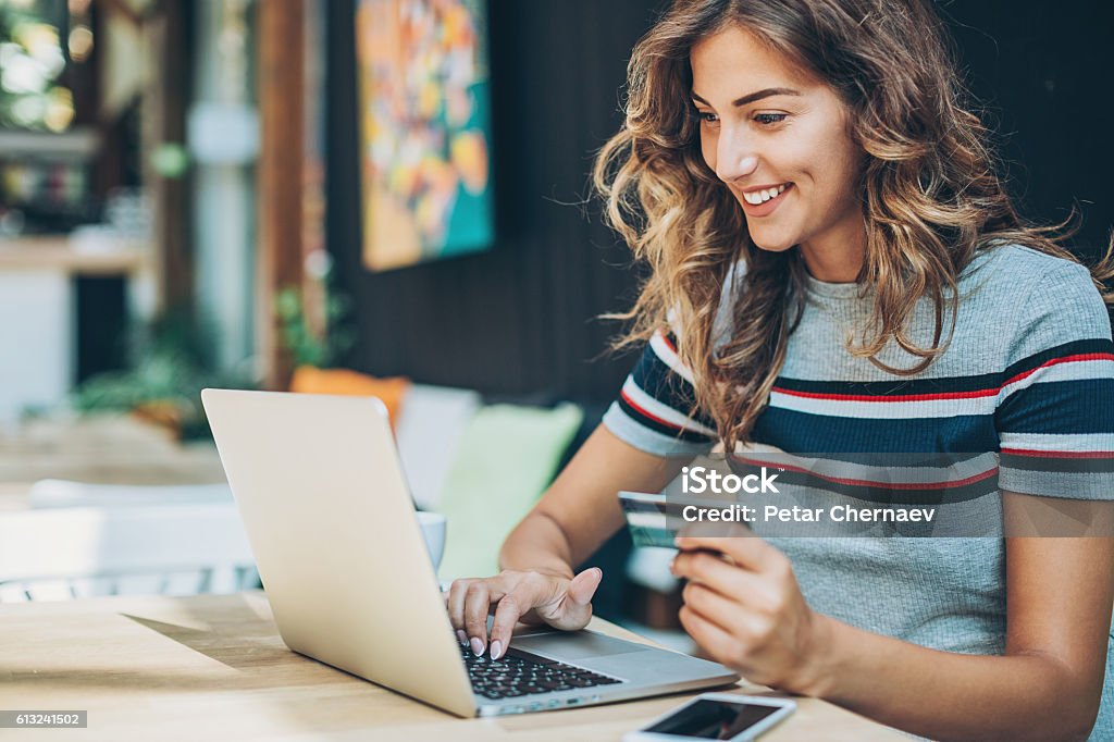 Young woman shopping on-line Smiling young woman holding a credit card and typing on a laptop. Internet Stock Photo