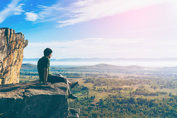 istock Young man in green sportswear is sitting on cliff's edge 613242350