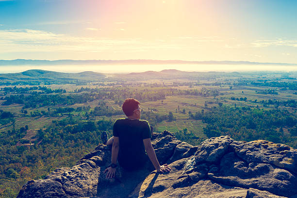 istock Young man in green sportswear is sitting on cliff's edge 613243564