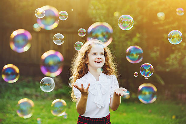Children playing in a park and blowing bubbles in summer
