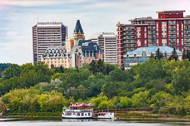 Horizontal image of Saskatoon cityscape along the South Saskatchewan River.  Image taken in early fall just as some of the tree leaves are beginning to change colour  Several hotels and condominiums can be seen in the image.  A tour boat that plies the river can be seen tied up in the foreground.