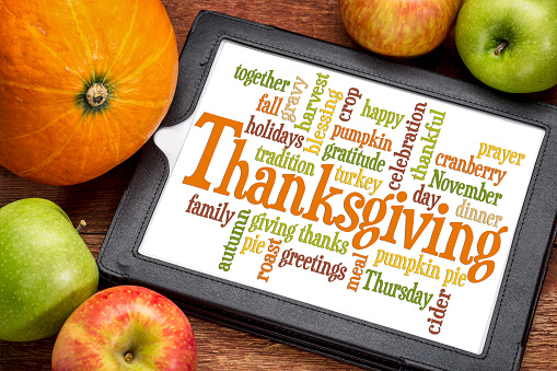 Thanksgiving word cloud on a digital tablet surrounded by pumpkin and apples