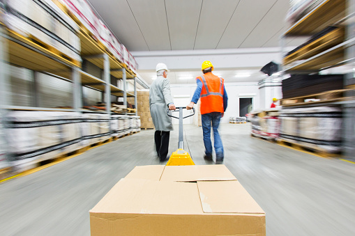 Two warehouse workers pulling pallet truck with boxes.....blurred motion