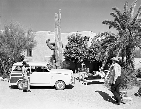 Tucson, Arizona, USA - March 31, 1948: Woman getting into a 1948 Crosley station wagon at Hacienda del Sol resort in the Sonoran desert near Tucson, Arizona. Resort guests relax while admiring the car. Scanned film.