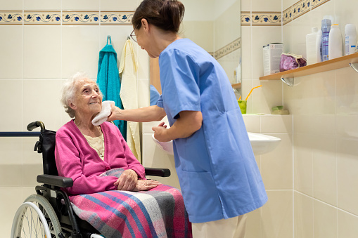 Home Caregiver with senior woman in bathroom, senior woman sitting in a wheelchair