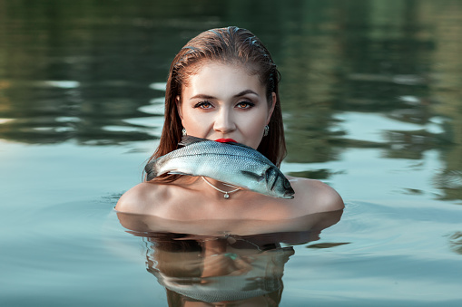 Girl stands in the water and holding a fish in his mouth.
