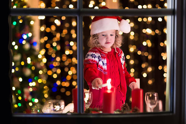 Christmas dinner at home. Child lighting a candle on advent wreath on Xmas eve. Decorated living room with fireplace and tree. Winter evening at fire place for family with kids. Children celebrating.