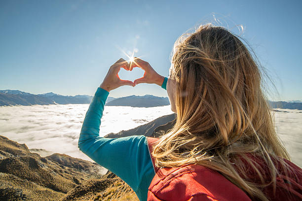 istock Woman on mountain top makes heart shape on sky 613318924