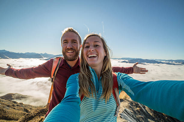 istock Young couple on mountain top take selfie above clouds 613318994
