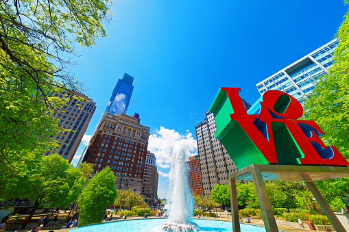 Philadelphia, United States - May 4, 2015: Love sculpture in the Love Park in Philadelphia, Pennsylvania, USA. People in the park. Skyline with skyscrapers on the background