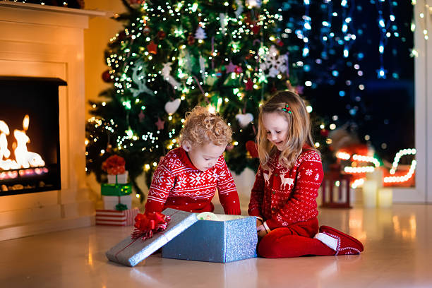 istock Little kids opening Christmas presents at fireplace 613324462