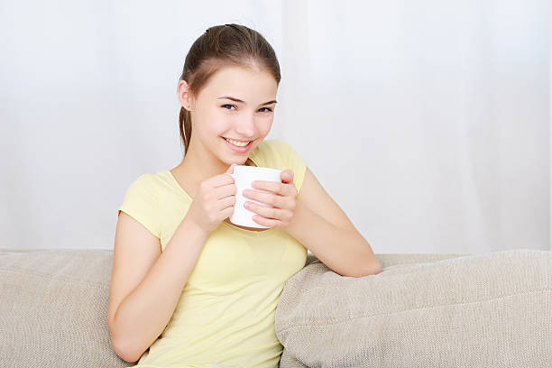 istock young woman sitting on couch and drinking coffee 613335386