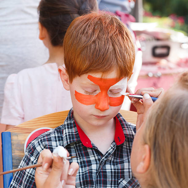 istock Child boy face painting, making tiger eyes process 613341532