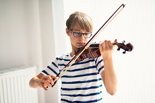 Teenage girl aged 10 is practicing violin in her room.
