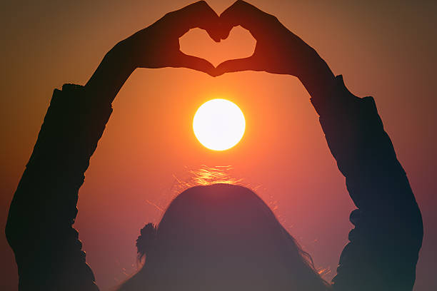 istock Girl making a heart-shape for the sunset. 613517534
