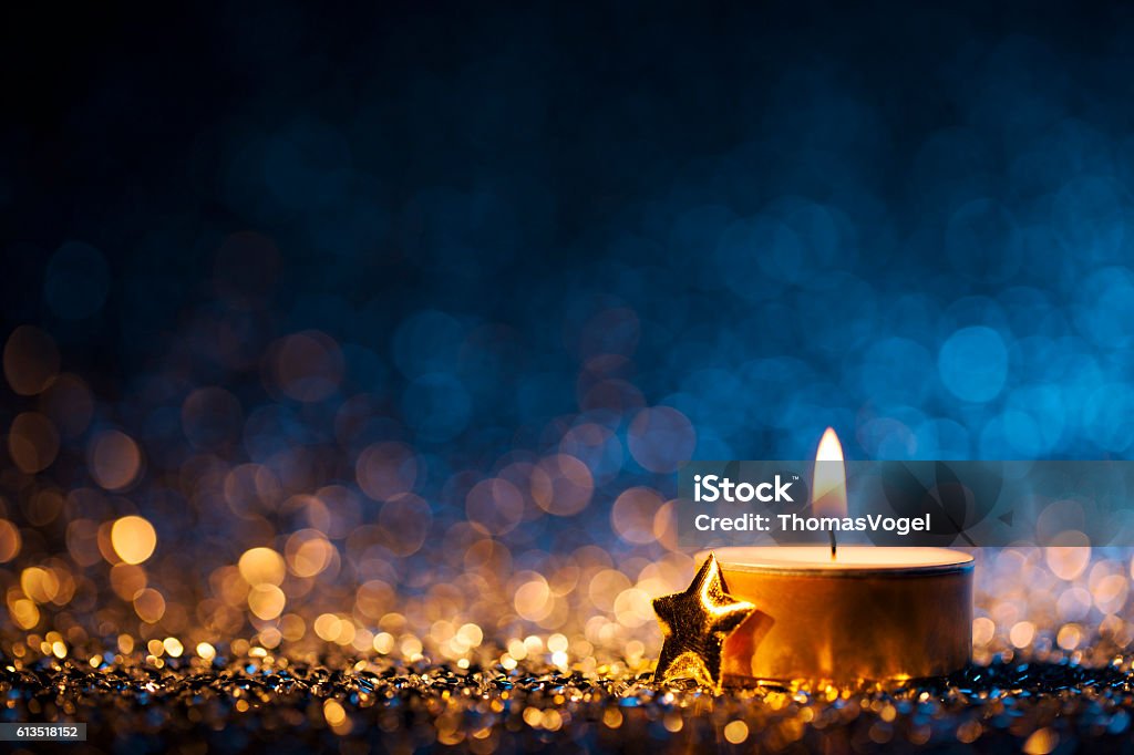 Lighted candle on defocused blue background - Christmas Tea Light Tea light and a golden star on defocused blue and gold background. Candle Stock Photo