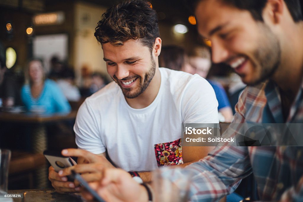 Two Friends Talking in a Cafe Two male friends talking and using smartphones in a cafe. Friendship Stock Photo