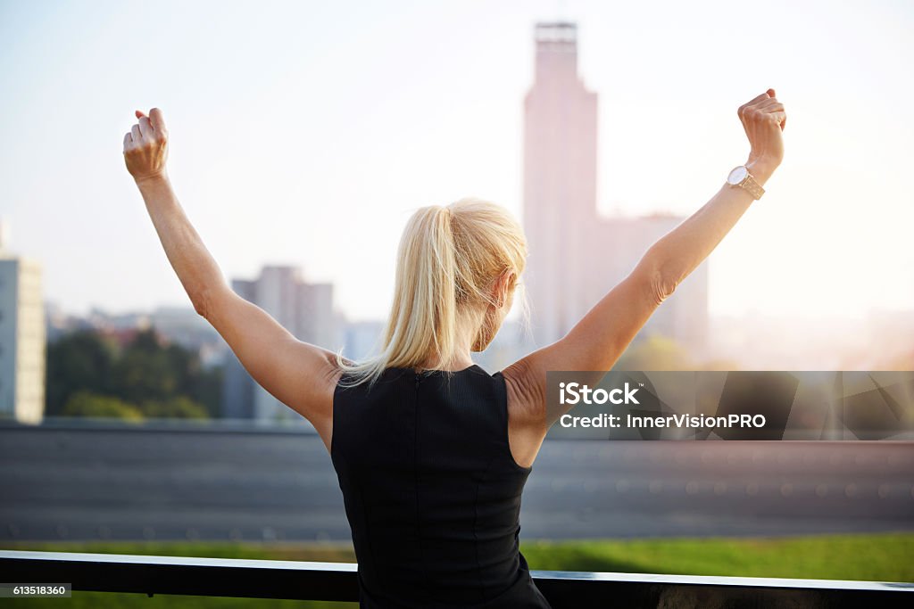 Successfull woman Back portrait of businesswoman standing front to the city view and raising hands in victory gesture. Women Stock Photo