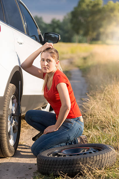 istock Sad young woman replacing car tire at field 613520532