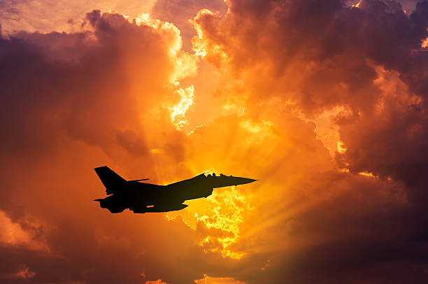 silhouette f-16 militärflugzeug fliegt bei sonnenuntergang - jagdflugzeug stock-fotos und bilder