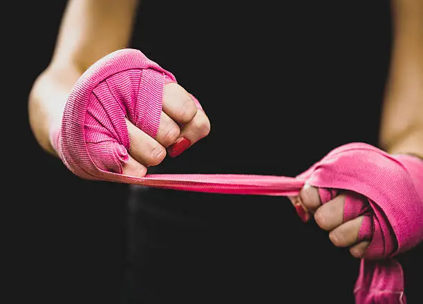 Woman is wrapping hands with pink boxing wraps. Isolated on black with red nails. Strong hand and fist, ready for fight and active exercise. Matte wash image