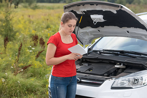 istock Woman standing at broken car and reading owner manual 613523000