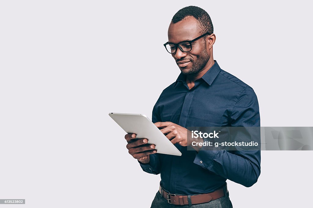 Business expert at work. Handsome young African man working on digital tablet while standing against grey background Men Stock Photo