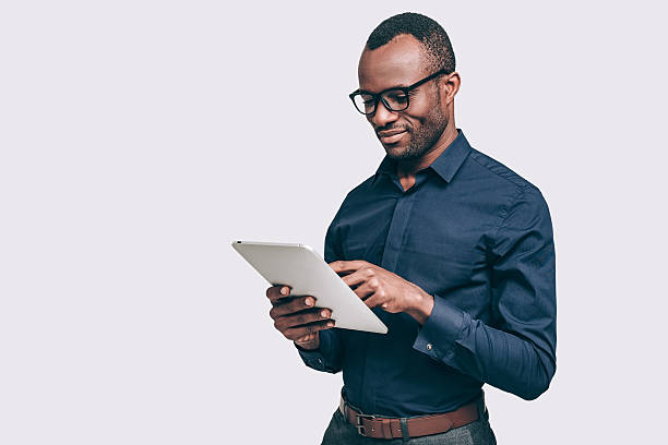 Business expert at work. Handsome young African man working on digital tablet while standing against grey background using digital tablet stock pictures, royalty-free photos & images