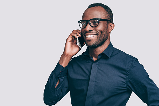 Handsome young African man talking on smart phone and smiling while standing against grey background