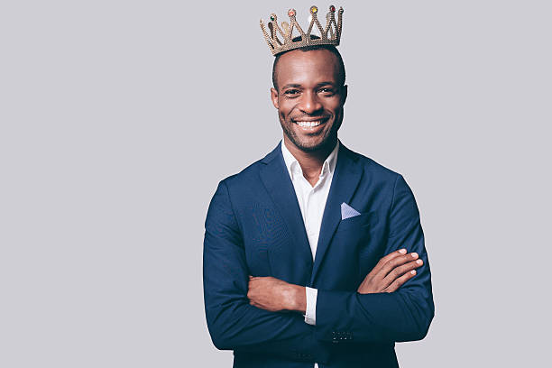 Like a king. Handsome young African man in crown and smart casual jacket looking at camera and smiling standing against grey background king royal person stock pictures, royalty-free photos & images