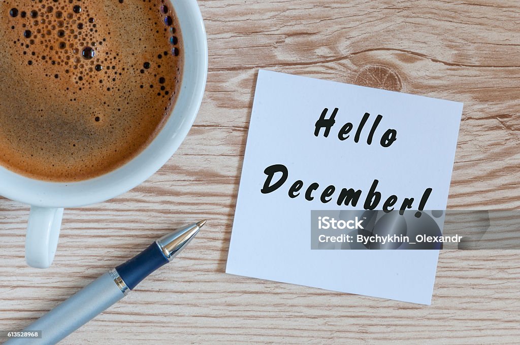 Hello December written on paper near morning coffee cup at Hello December written on paper near morning coffee cup at manager or freelancer workplace. Eve, Christmas and New year time concept. December Stock Photo