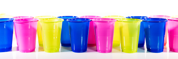 Many colorful plastic cups, lined up in front of white