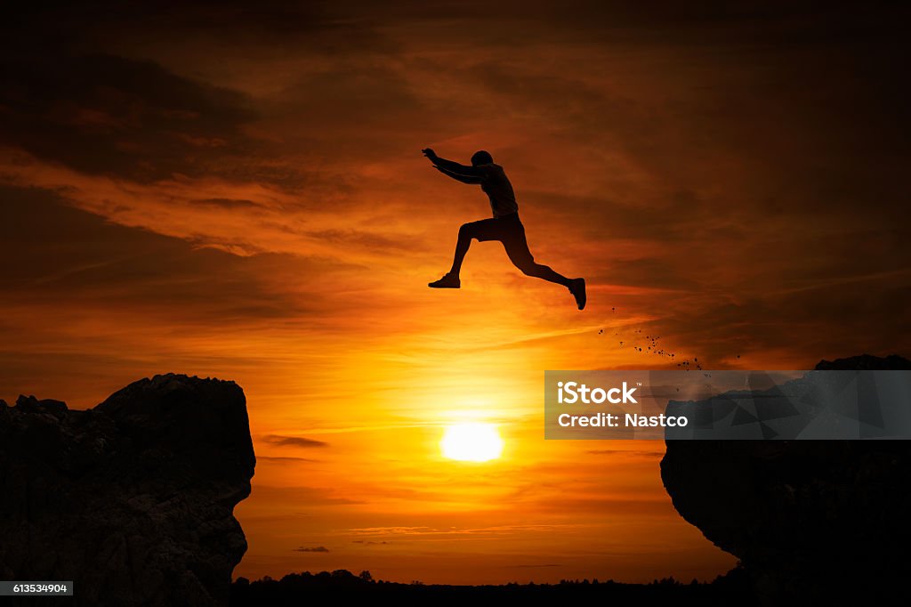 Jumping over abyss Silhouette of a man jumping over abyss at sunset with copy space Jumping Stock Photo