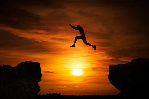 Jumping over abyss Silhouette of a man jumping over abyss at sunset with copy space ravine stock pictures, royalty-free photos & images