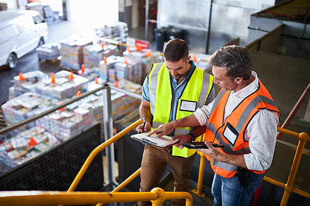 Double checking their shipping schedule Shot of two warehouse workers standing on stairs using a digital tablet and looking at paperwork distribution warehouse stock pictures, royalty-free photos & images