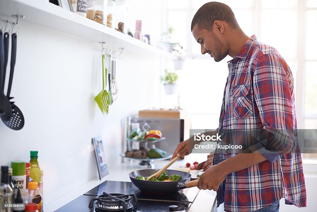 Cooking up something good in the kitchen Shot of a young man cooking over a stove in his kitchen Cooking Stock Photo