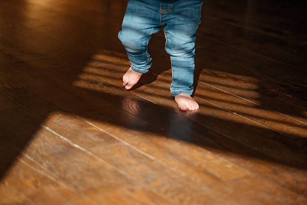 los primeros setps del bebé dentro de una casa en un día soleado - child human foot barefoot jeans fotografías e imágenes de stock